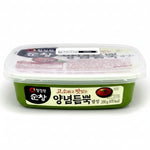 A container of Korean food, specifically Yangnamdumppok (pickled red cabbage), in a green plastic tub with a clear lid. The packaging features a white and green label with Korean text and a red cabbage illustration.