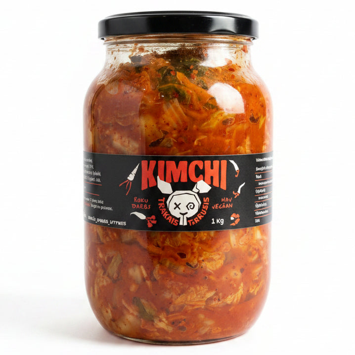 A large glass jar of Kimchi Korean fermented cabbage on a white refrigerator shelf. The jar has a black lid and a black label with red and white text reading 'KIMCHI' and a cartoon cow graphic.